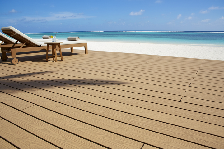 4 Everdeck® Sandal Wood deck with lounge chairs and a table overlooking a beach and ocean.