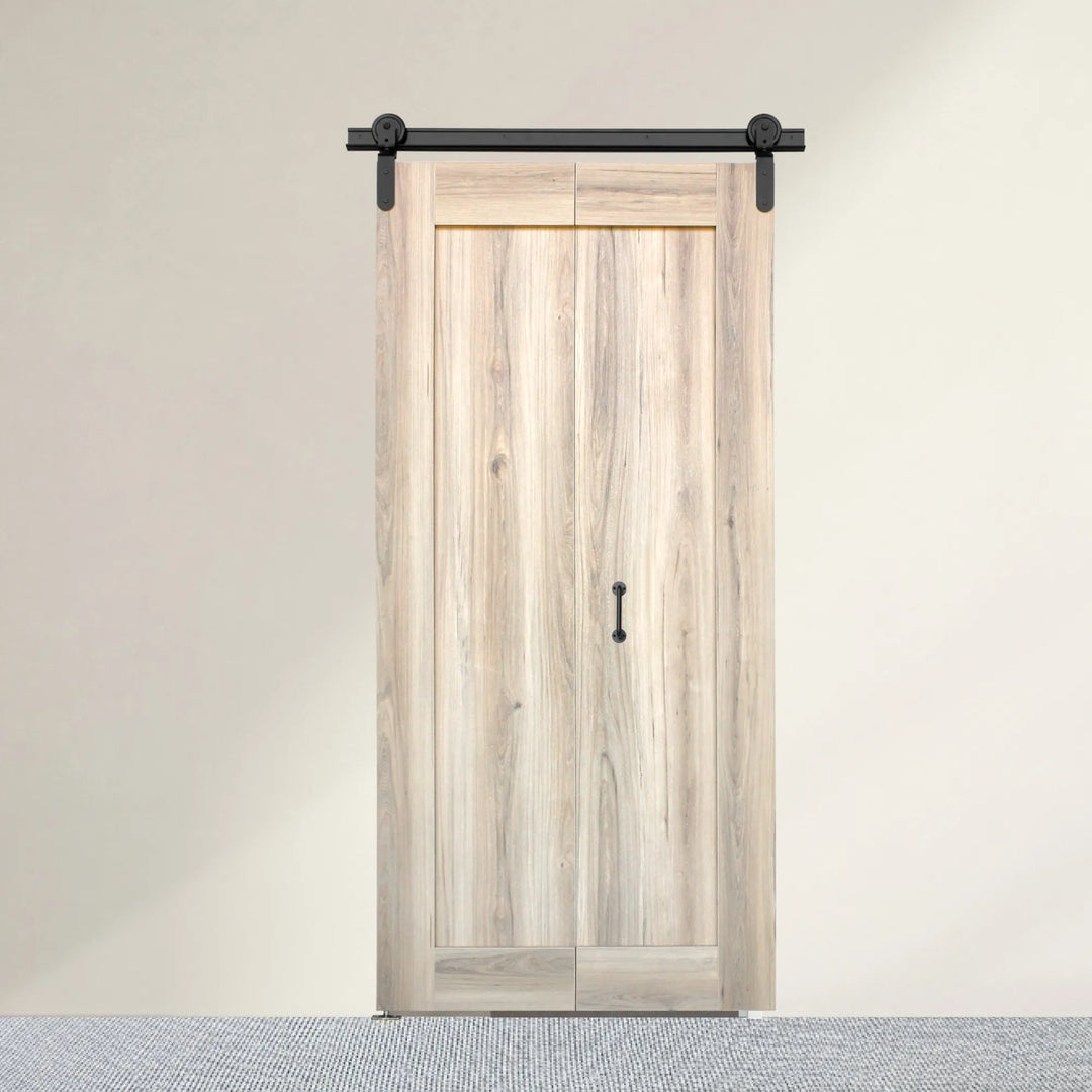 Sahara bi-fold barn door closed — light Sahara wood-grain melamine finish with black barn-style handle and top-hung sliding track shown against a neutral beige wall and textured gray floor.